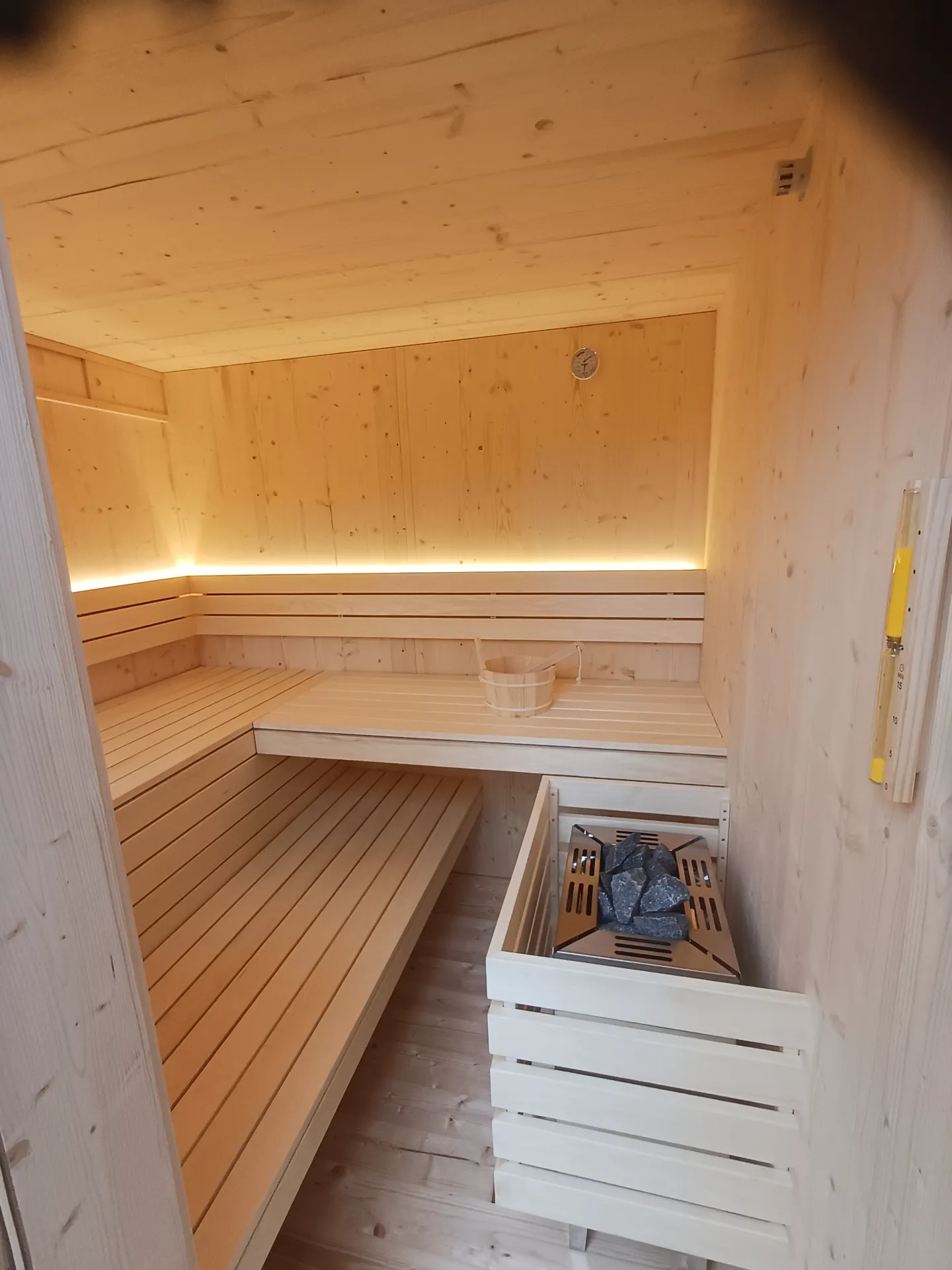 Innenraum der Außensauna mit indirekter LED-Beleuchtung, Saunaofen und Aufgusskübel